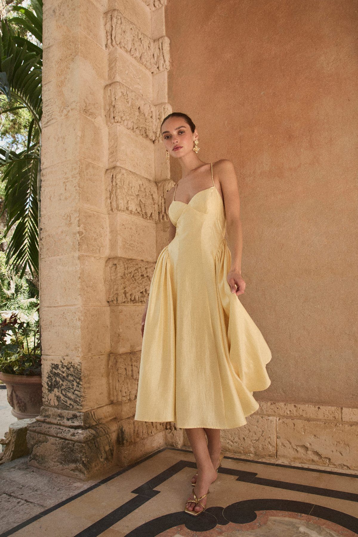 Woman wearing a pale yellow linen midi dress standing by a stone pillar outdoors.