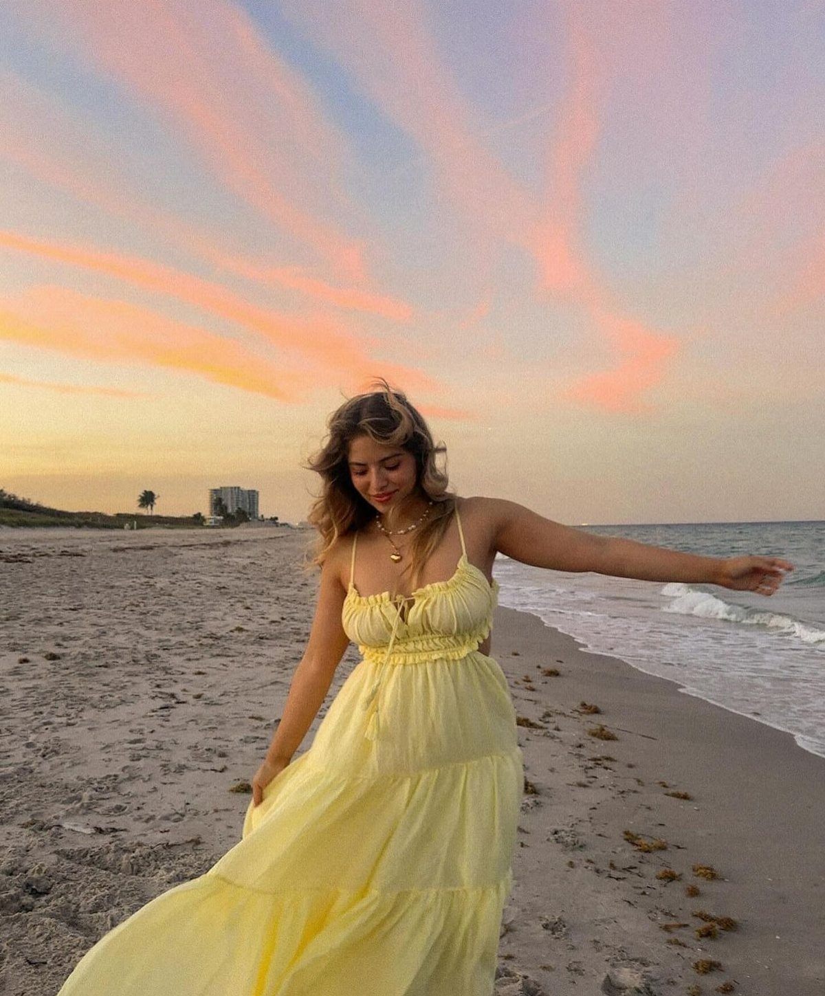 A woman in a pale yellow tiered maxi dress standing on a beach at sunset.